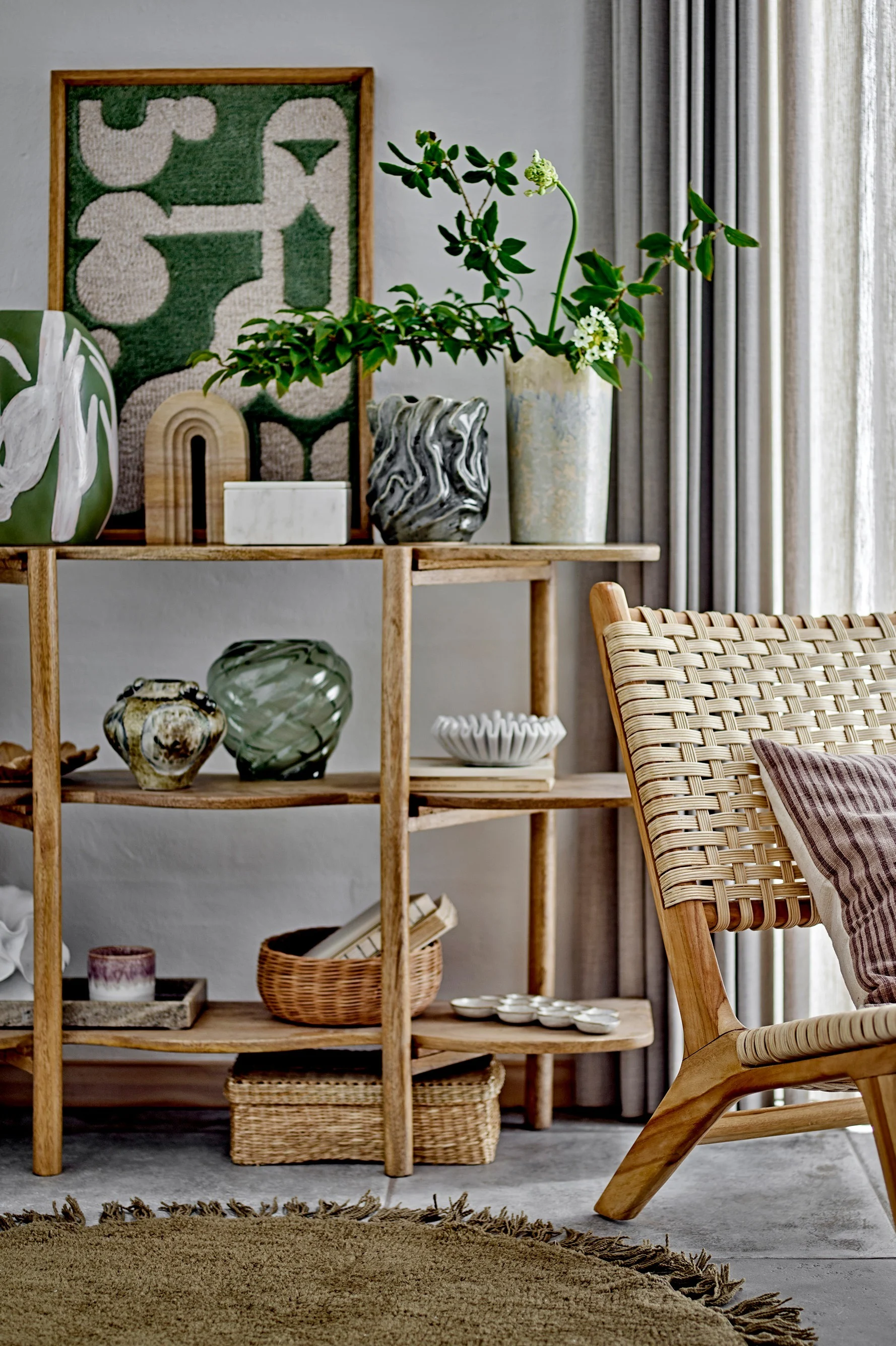 Ein im Boho Style eingerichtetes Wohnzimmer mit einem Sessel, einem dekorierten Regal und der Longton Wanddekoration von Bloomingville.