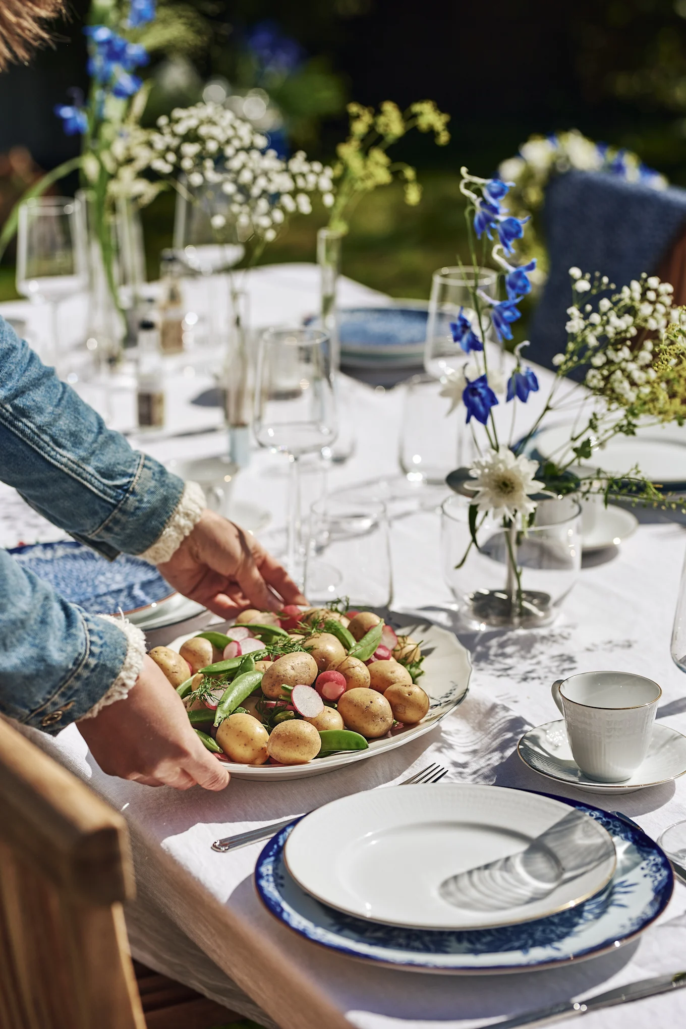 Midsommar wird in Schweden mit frischen Gerichten gefeiert, hier wird ein Teller mit Kartoffelsalat auf den blau-weiß gedeckten Tisch gestellt.