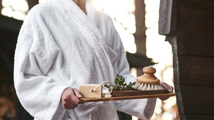 Ein Tablett mit Raumzubehör wie Seife und Bürste wird in die Sauna getragen, um einen Moment der Entspannung zu genießen. 