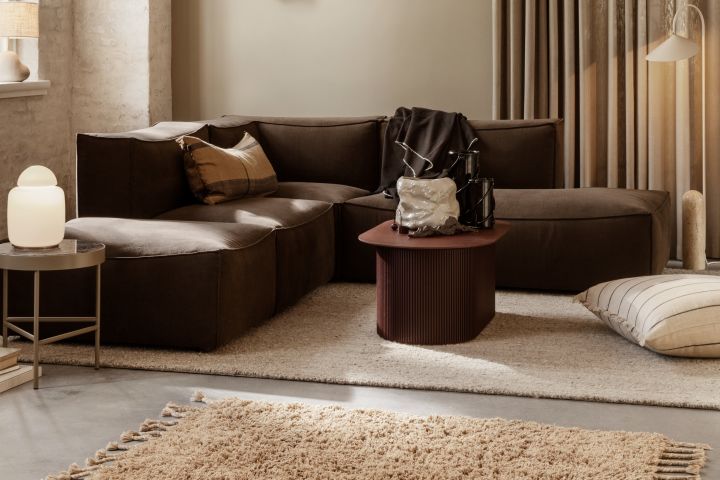 Wohnzimmer in herbstlichen Farbtönen mit dunkelrotem Tisch, beigefarbener Lampe und Kissen von Ferm Living – Komponenten, welche die Herbsttrends 2021 widerspiegeln.