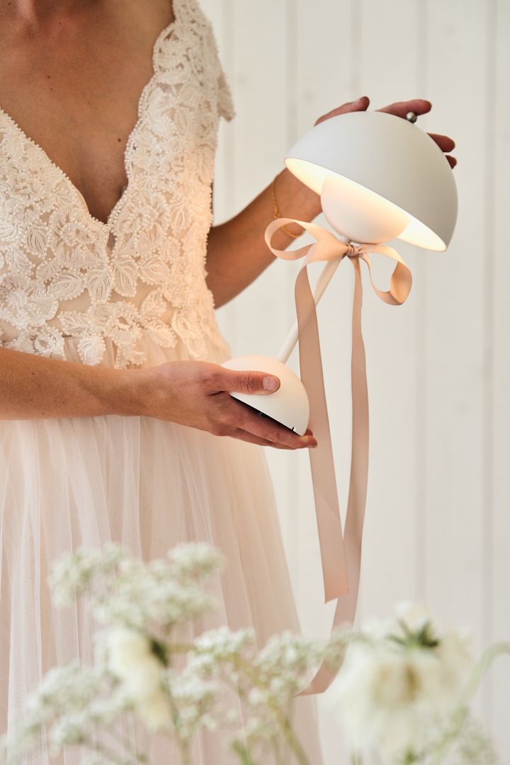 Hier sehen Sie eine Braut, die eine weiße tragbare VP9 Flowerpot-Tischlampe in der Hand hält. Planen Sie bei Ihrer Hochzeit unbedingt einen Geschenketisch ein!