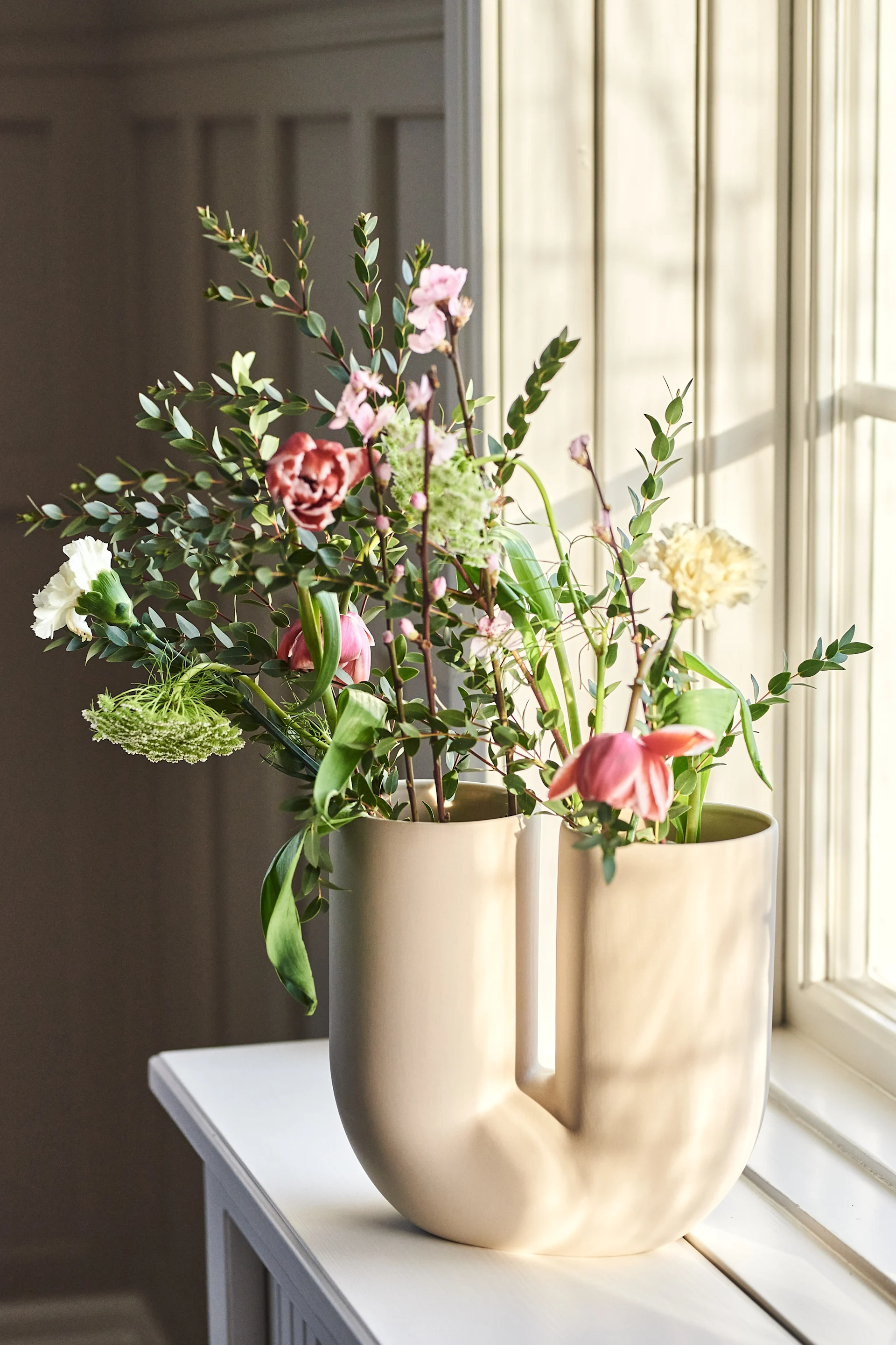Die Kink Vase in Beige von Muuto auf der Fensterbank, darin bunte Frühlingsblumen.