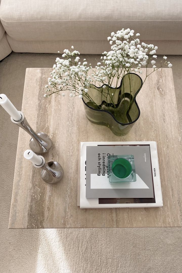 Gestalten Sie ein gemütliches Hygge-Wohnzimmer mit natürlichen Elementen wie einem Couchtisch aus Stein oder einer grünen Vase, hier sehen Sie die Alva Aalto Vase von Iittala. 
