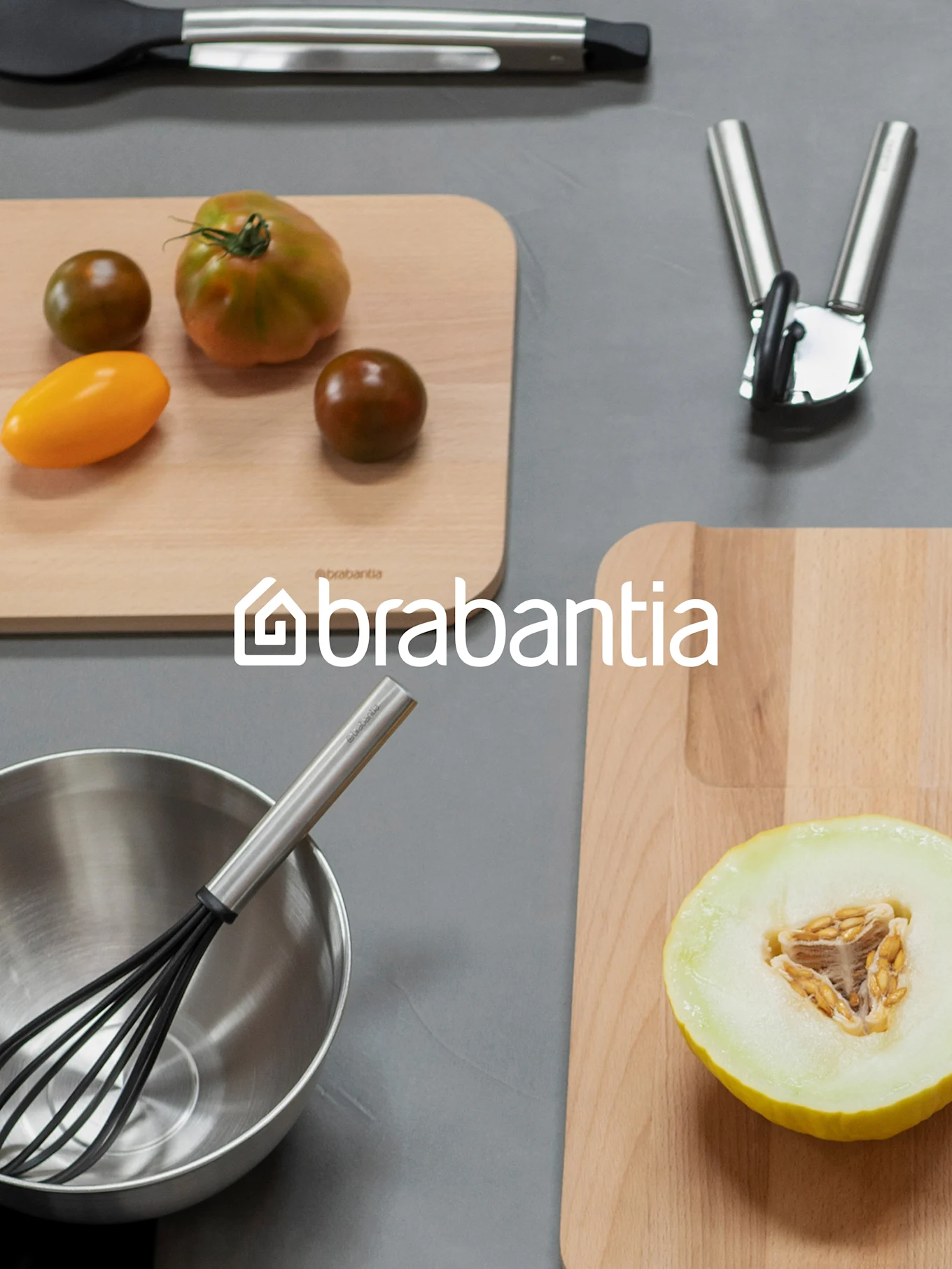 Brabantia-Logo über einer Aufsicht von Küchenartikeln, einschließlich Schneidebrettern mit Tomaten und Melone, einem Schneebesen in einer Schüssel und anderem Besteck.