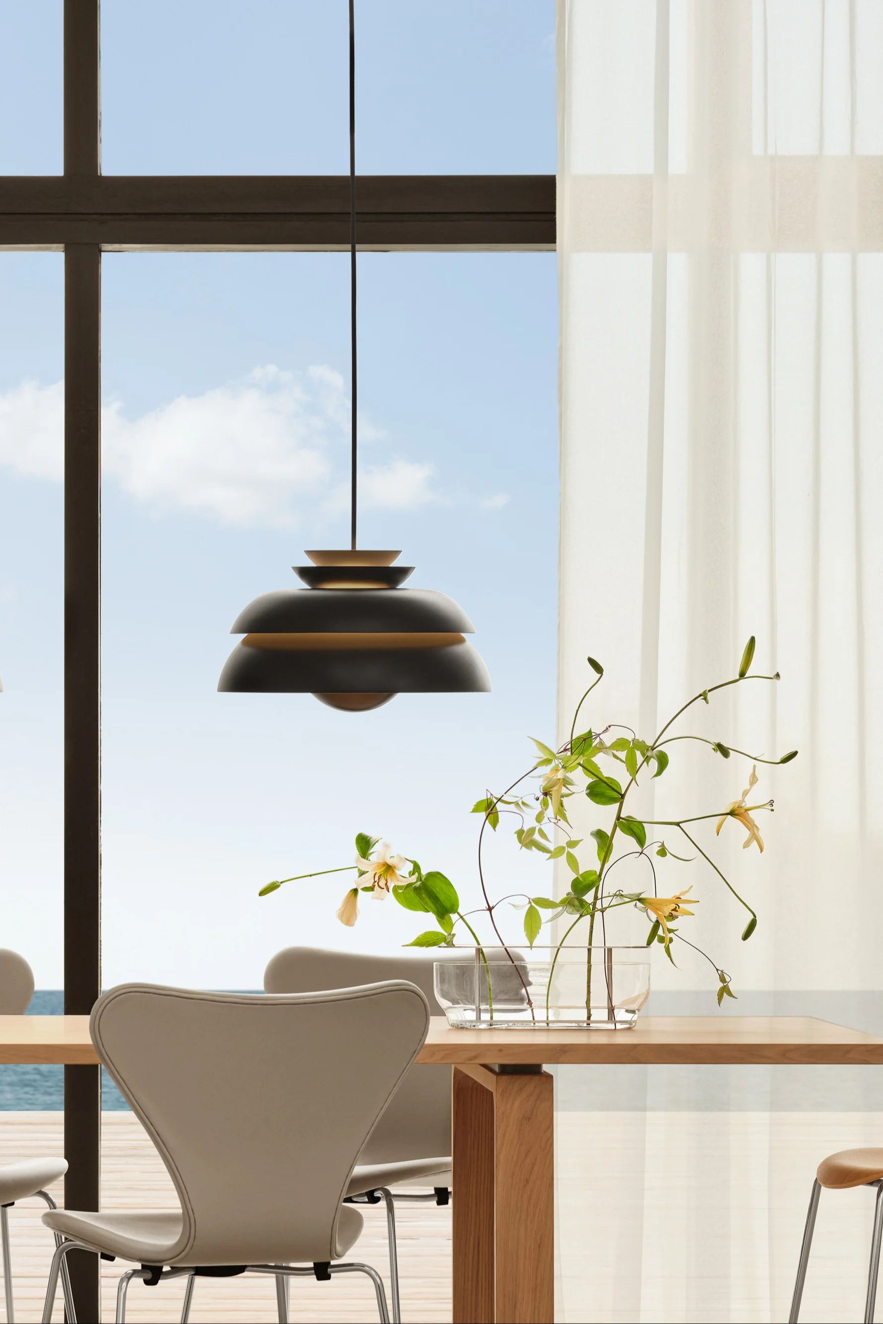 Esszimmer: Holztisch, Stühle, dunkle Pendelleuchten. Blumen. Fenster, transparente Vorhänge, Meerblick.