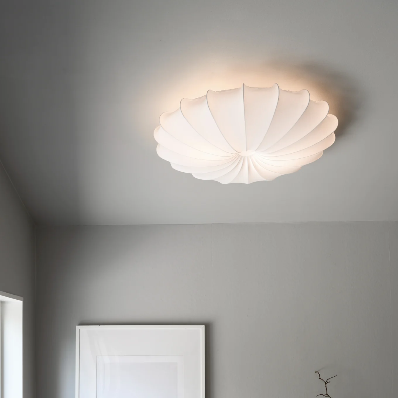 Eine weiße, plissierte, muschelförmige Deckenlampe beleuchtet eine graue Decke.