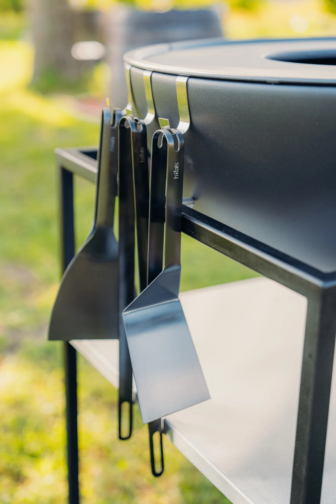Drei schwarze Spatel mit Höfats-Logo hängen an einem schwarzen Außengrill.