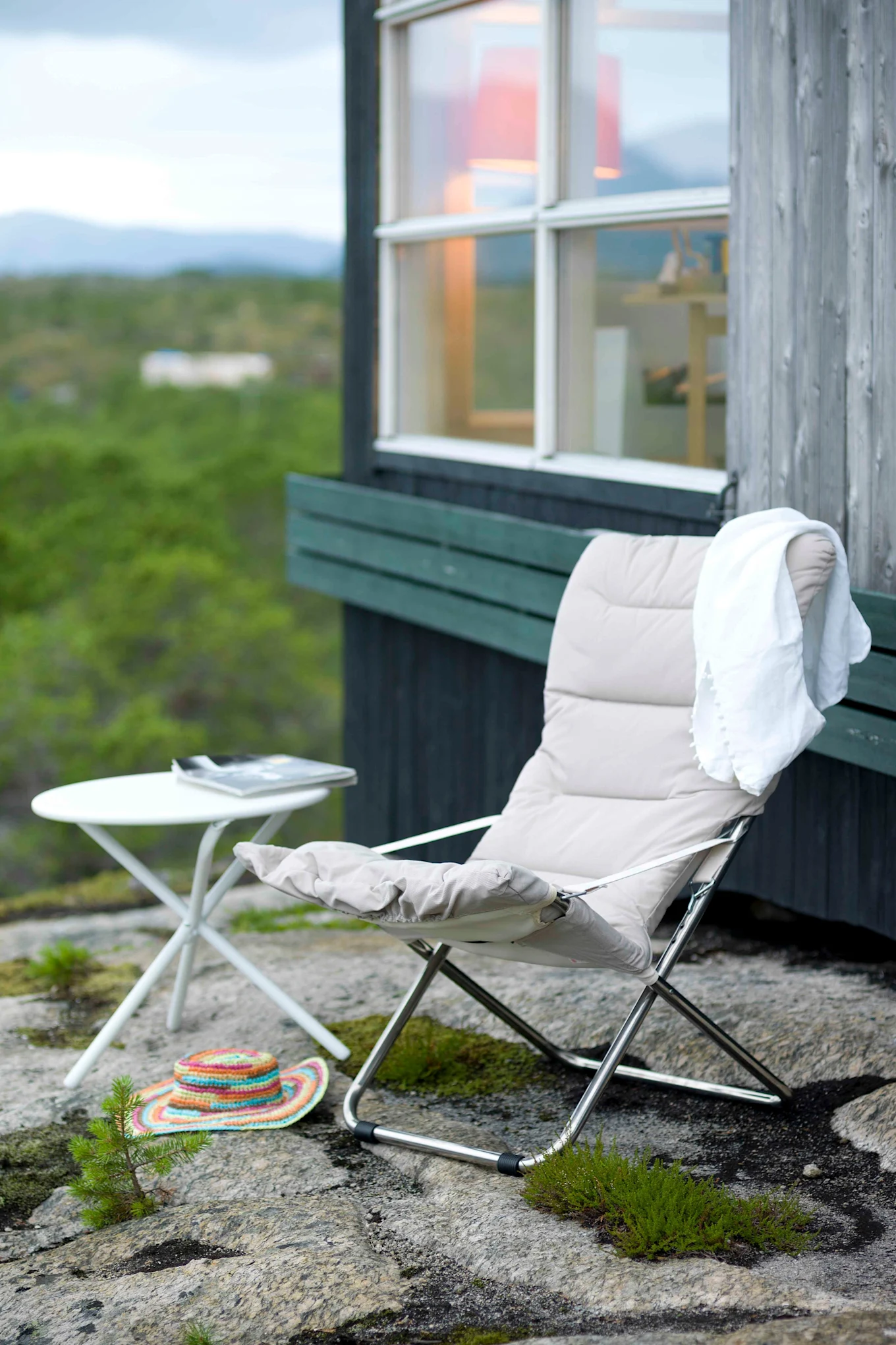 Die Fiesta Soft Sonnenliege von Fiam steht auf einer Terrasse, darunter erstreckt sich Wald. Du ihre einfache Klappbarkeit gehört sie zu den diesjährigen Gartenmöbeltrends.
