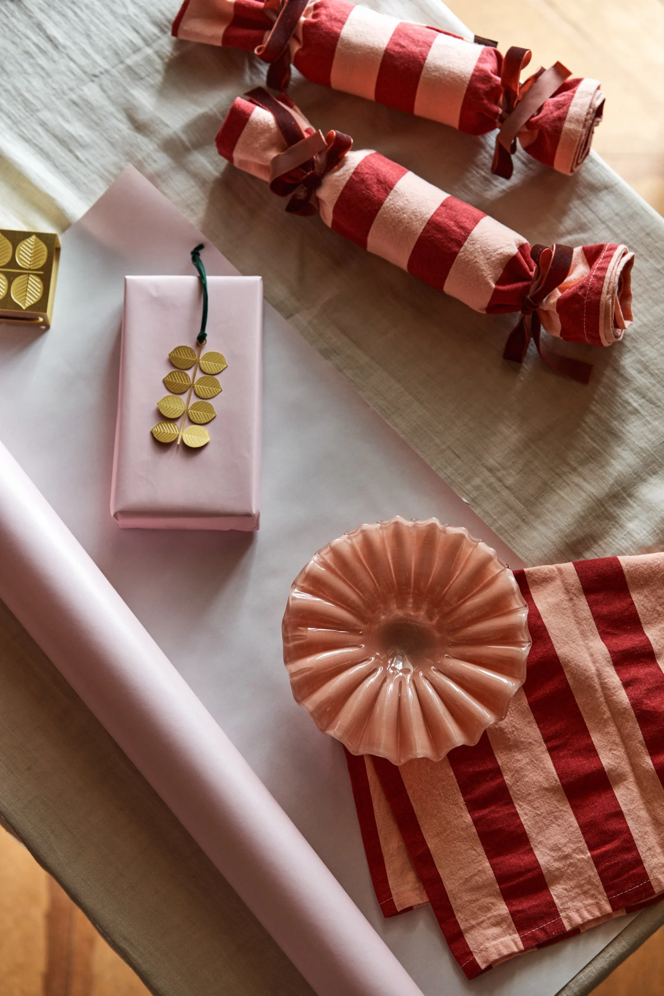 Hier warten eine rosa Schale von Byon und ein goldener Anhänger von Pluto darauf, schön in gestreifte Küchentücher und rosa Papier eingewickelt zu werden – eine kreative Art, den ersten Advent zu feiern.