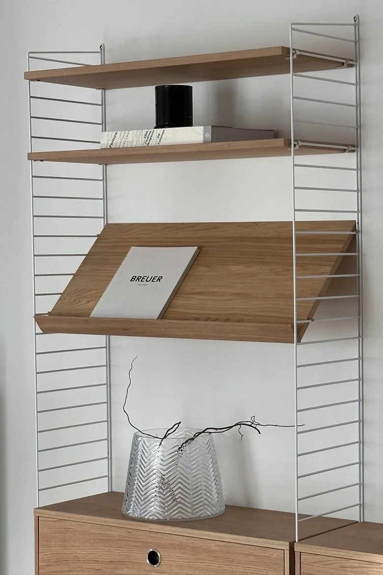 String Regalsystem: Hier sehen Sie ein weißes String-Gestell mit hölzernen Einlegeböden, dekoriert mit einer Vase.