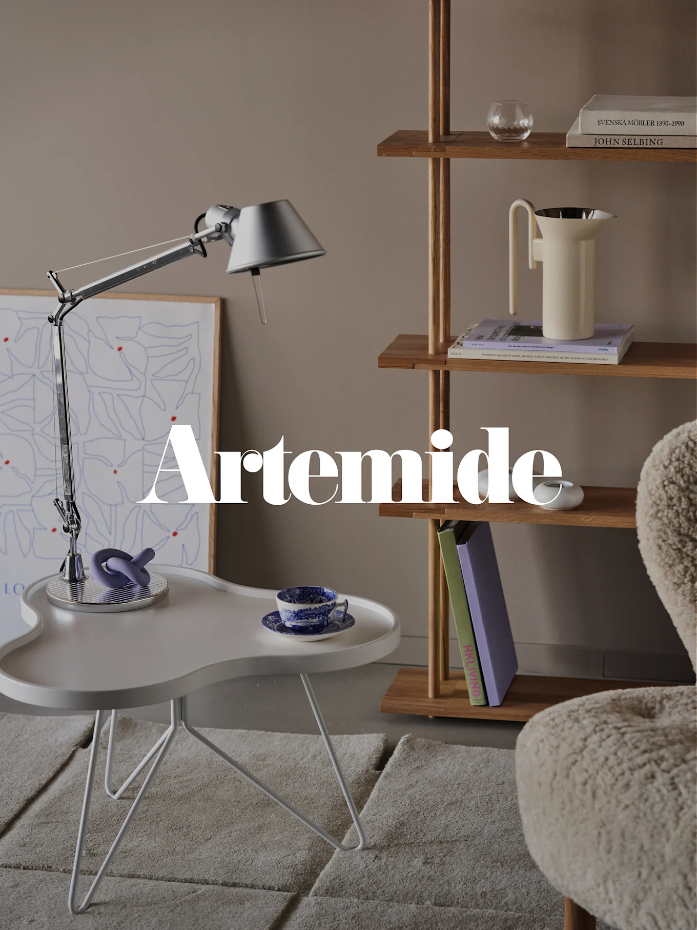 Ein modernes Wohnzimmer mit silberner Schreibtischlampe, weißem Beistelltisch, Holzregal und cremefarbenem Sessel. Textüberlagerung: 'Artemide'.
