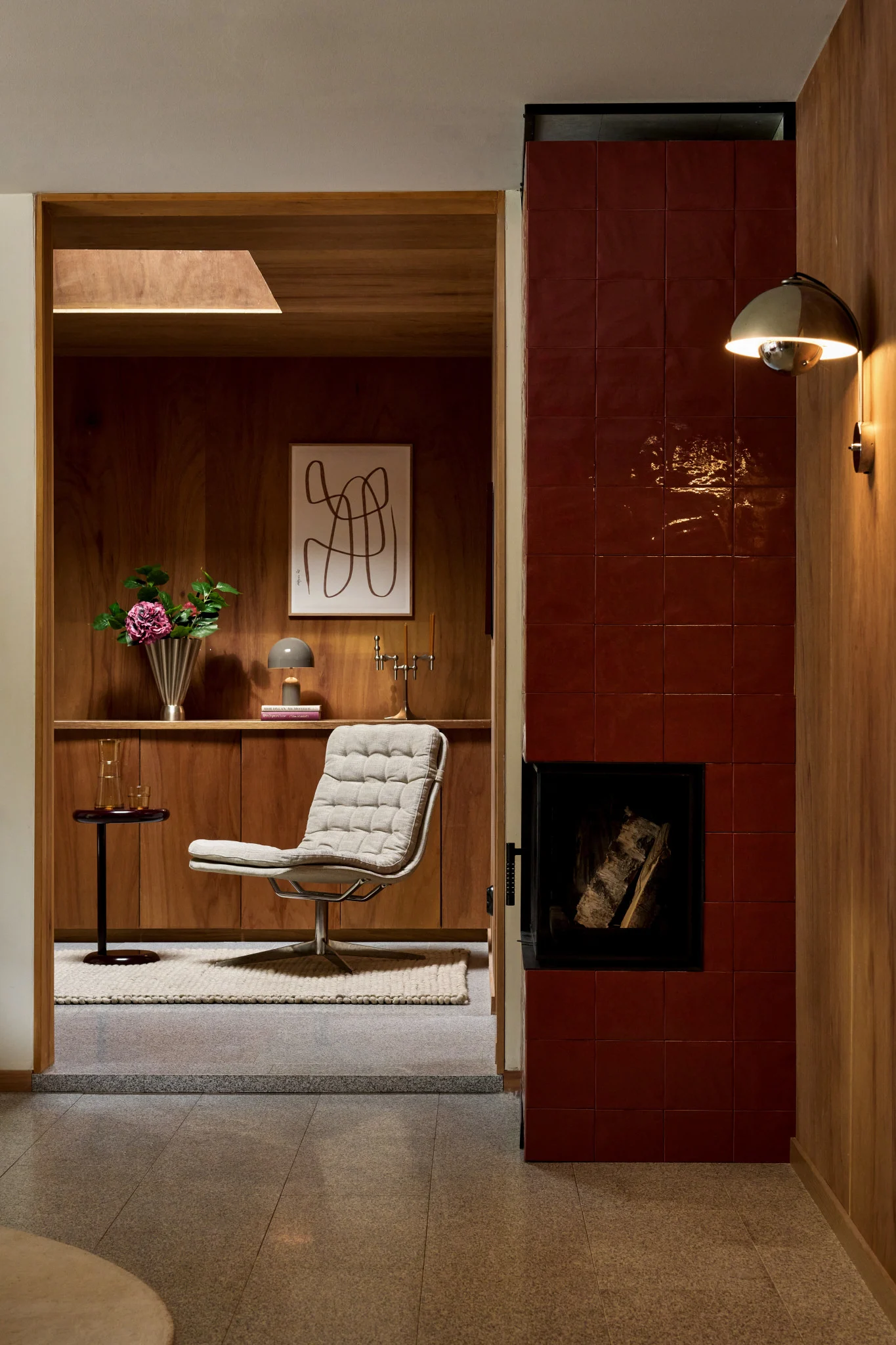 Ein gemütliches Interieur mit einem strukturierten Loungesessel, Holzvertäfelung, einem rot gefliesten Kamin und einer goldenen Wandleuchte.