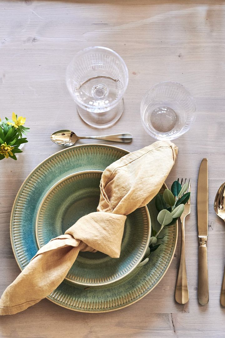Geknotete gelbe Leinenserviette auf grünen Tellern auf einer schönen Frühlingstafel - ein schöner Tipp, wie man Leinenservietten faltet und den Tisch damit deckt. 