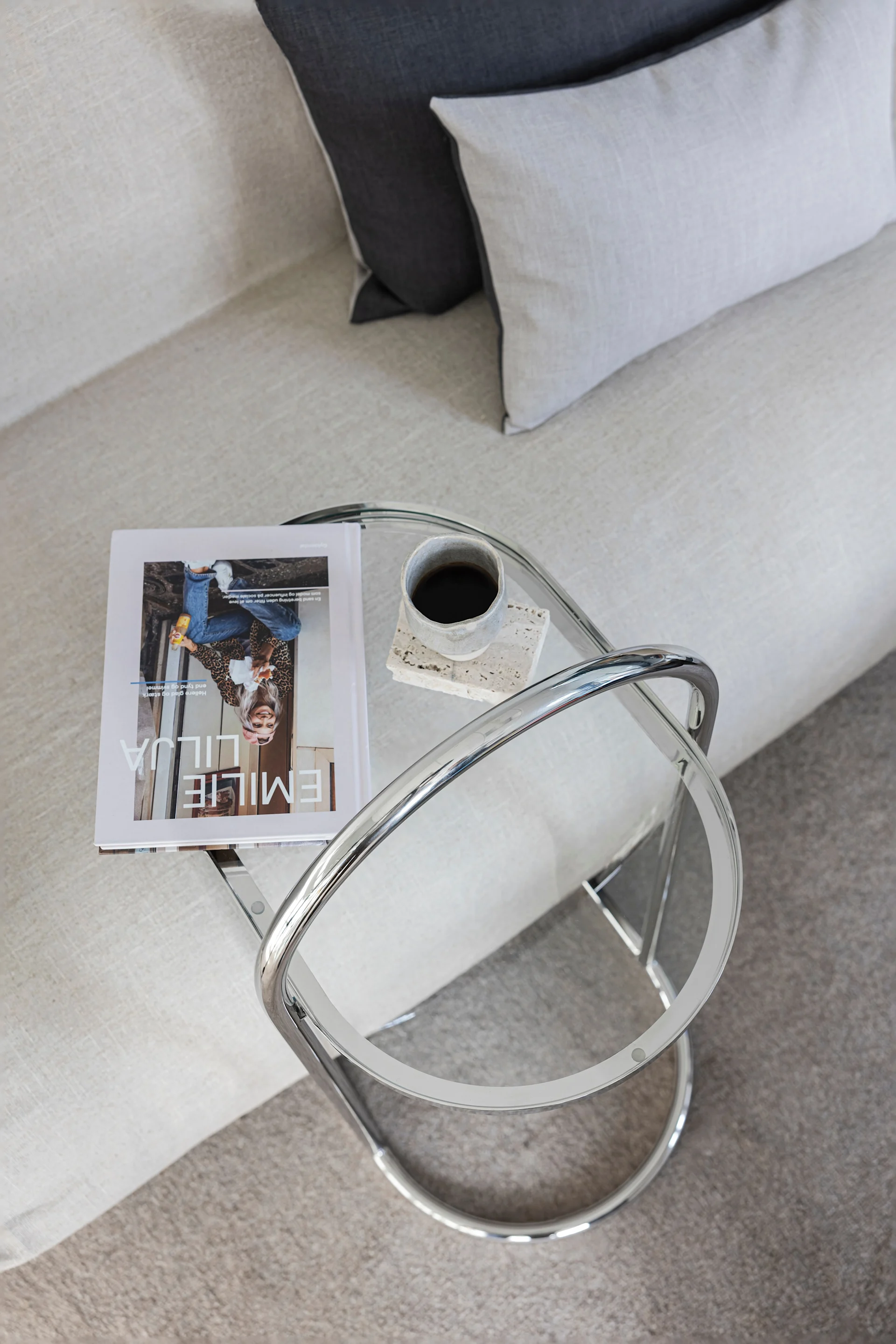 Blick von oben auf ein modernes Wohnzimmer mit hellem Sofa, Zierkissen und einem Beistelltisch aus Glas und Chrom mit Magazin und Kaffee.