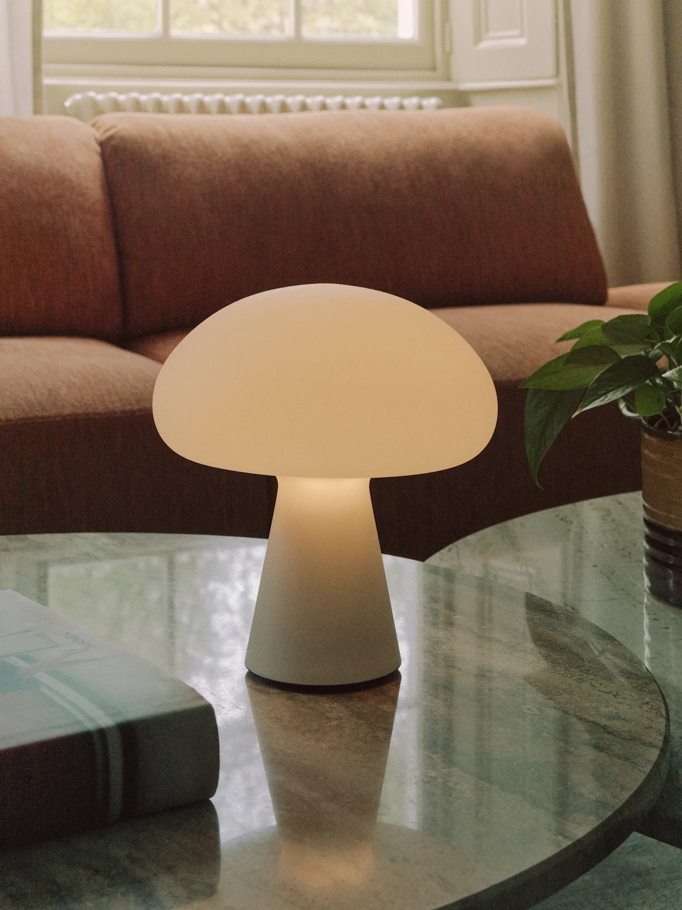 Eine cremefarbene Pilz-Tischlampe steht auf einem runden Marmor-Couchtisch in einem Wohnzimmer.