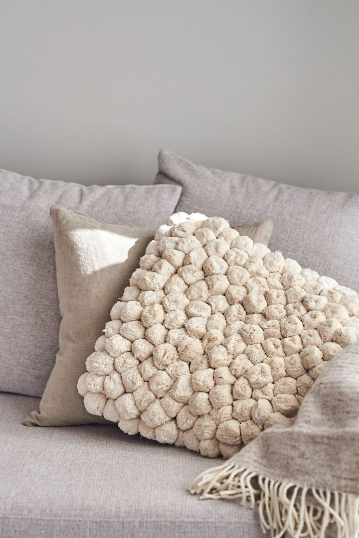 Dekorieren Sie Ihr Wohnzimmer mit beigen Ton-in-Ton-Möbeln, um eine stilvolle Atmosphäre in Ihrem Zuhause zu schaffen. Hier sehen Sie das trendige Pom Pom Kissen von By On in Beige.