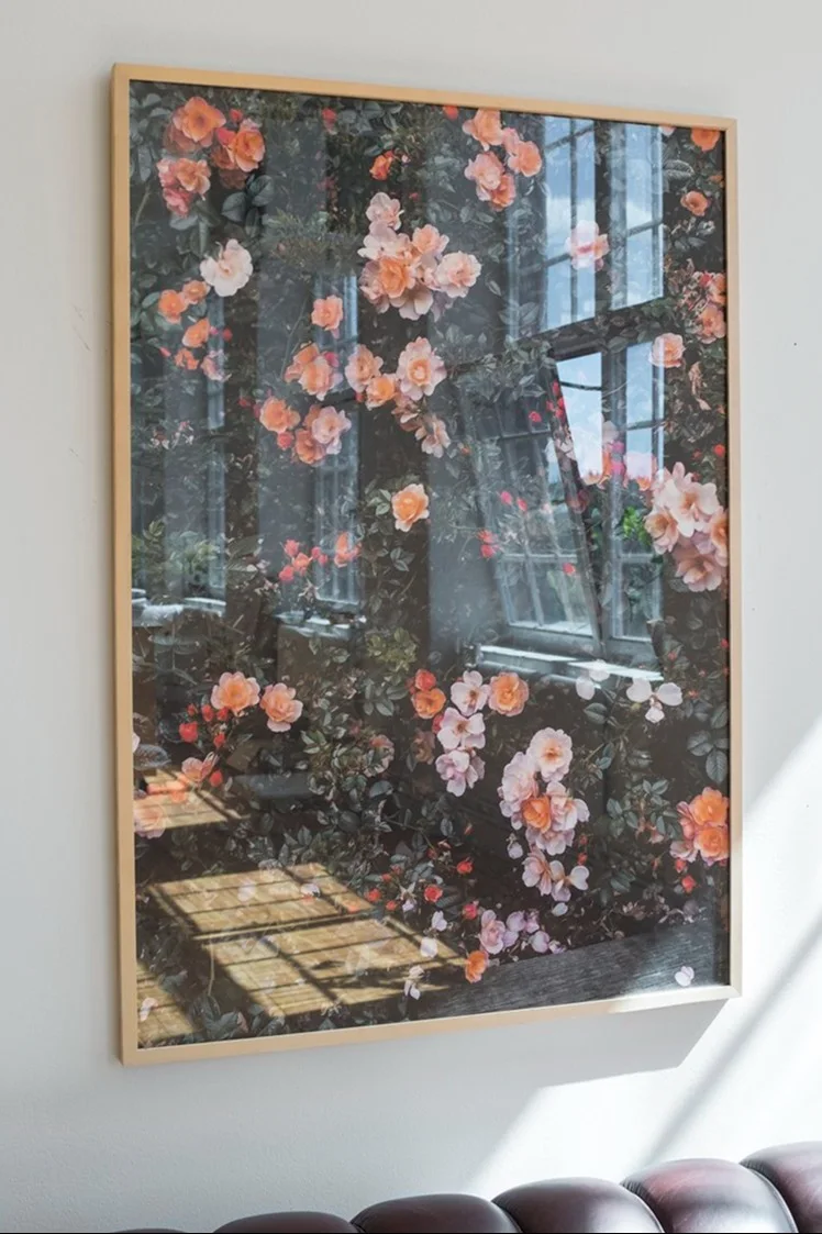 Gerahmter Druck eines üppigen Gartens mit Pfirsichrosen und Fensterreflexionen, an einer weißen Wand.