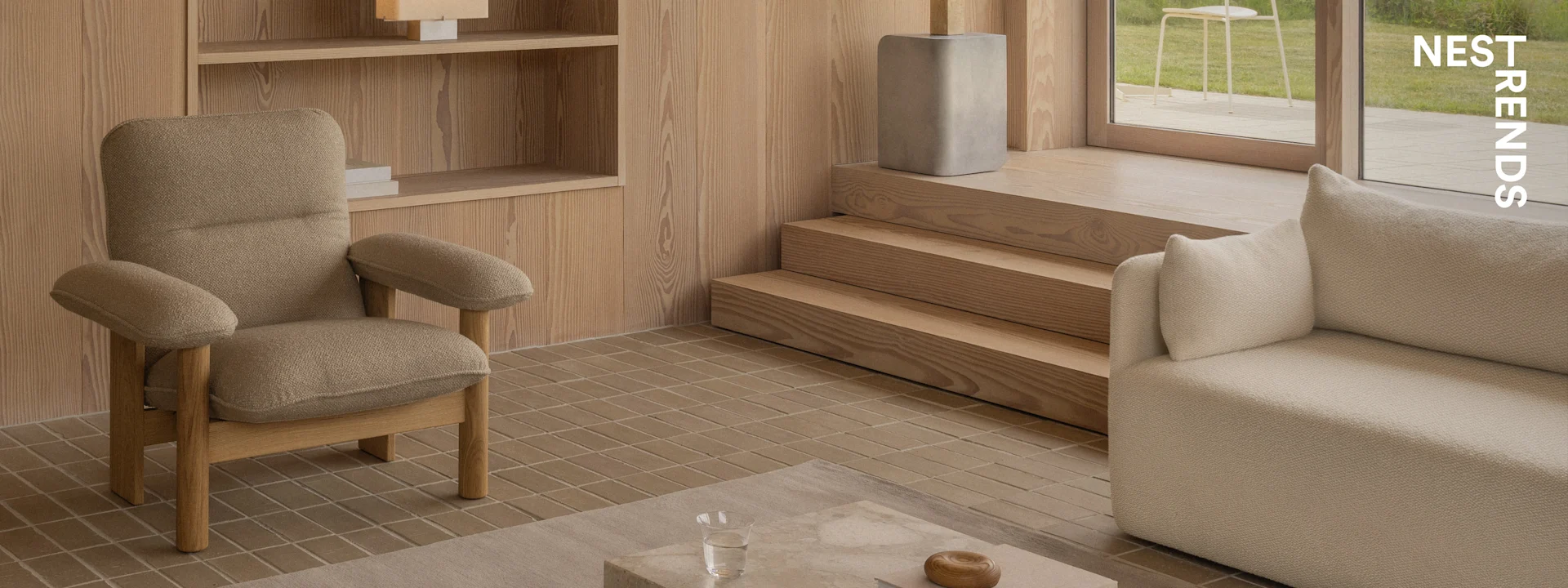 Ein modernes Wohnzimmer mit einem strukturierten braunen Sessel, einem beigen Sofa, Holzpaneelen, Fliesenboden und Blick auf einen Garten.