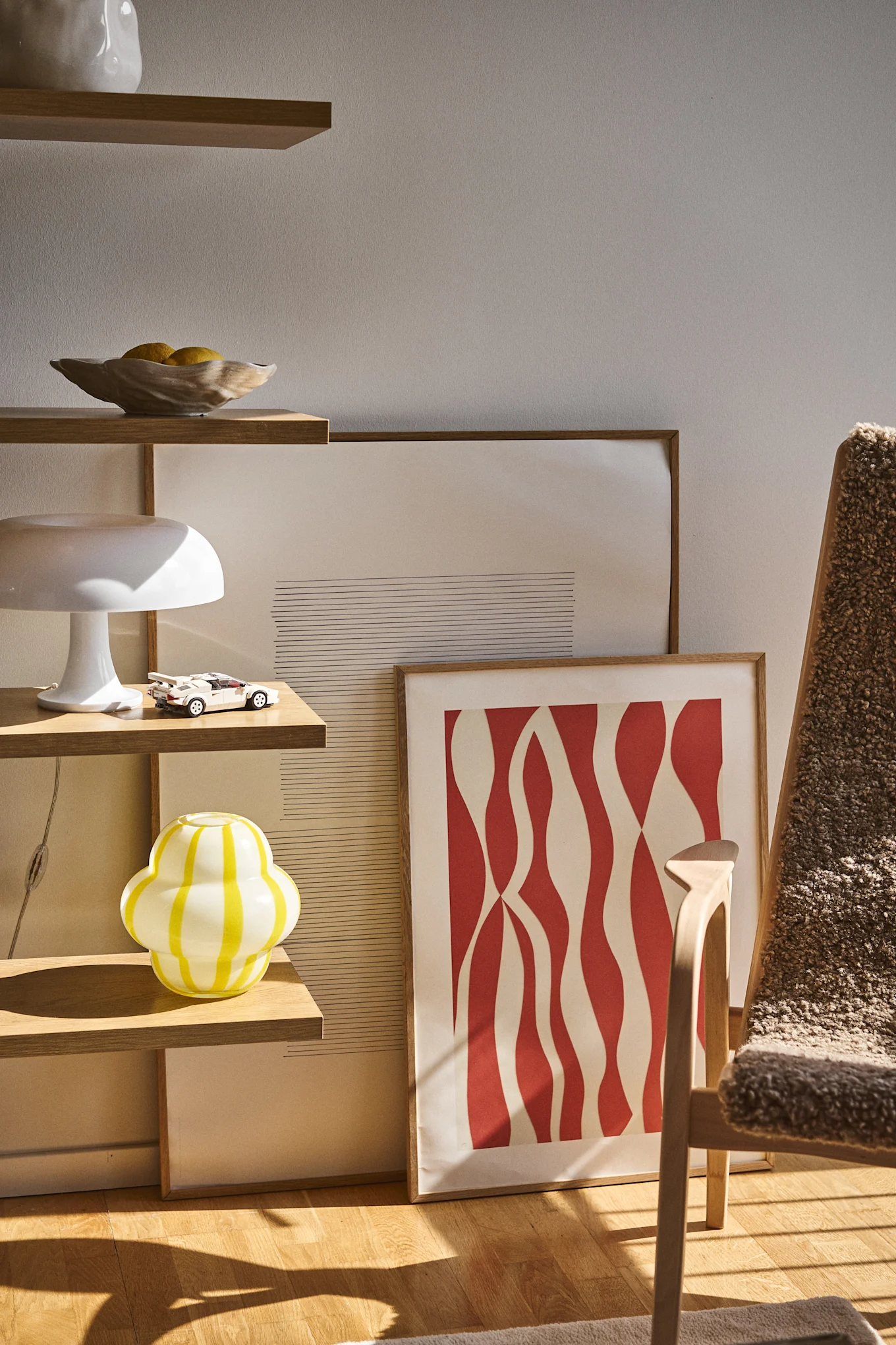 Die Curlie Vase von Byon hat ein rundes, bauchiges Design aus gelb und weiß gestreiftem Glas. Hier platziert in einem offenen Bücherregal zusammen mit Shell Schale, Lampen und Gemälden.