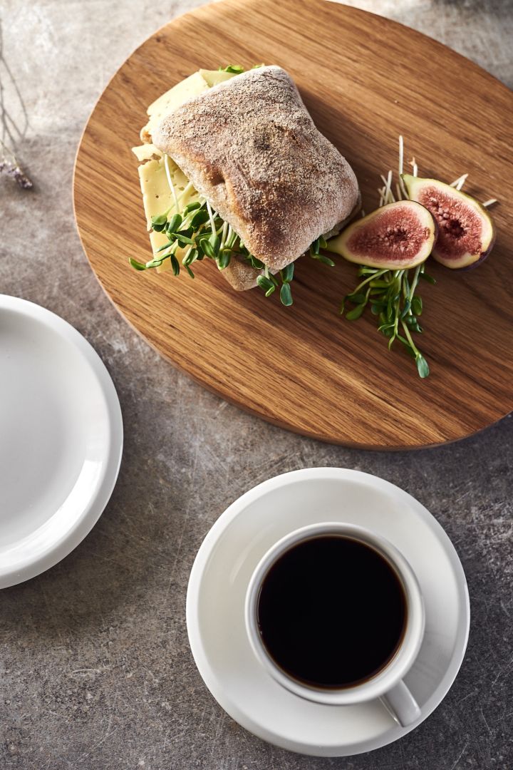 Kaffeetasse, kleiner Teller & Schneidebrett aus der Raami Serie von Iittala mit Kaffee und Frühstücksbrötchen.