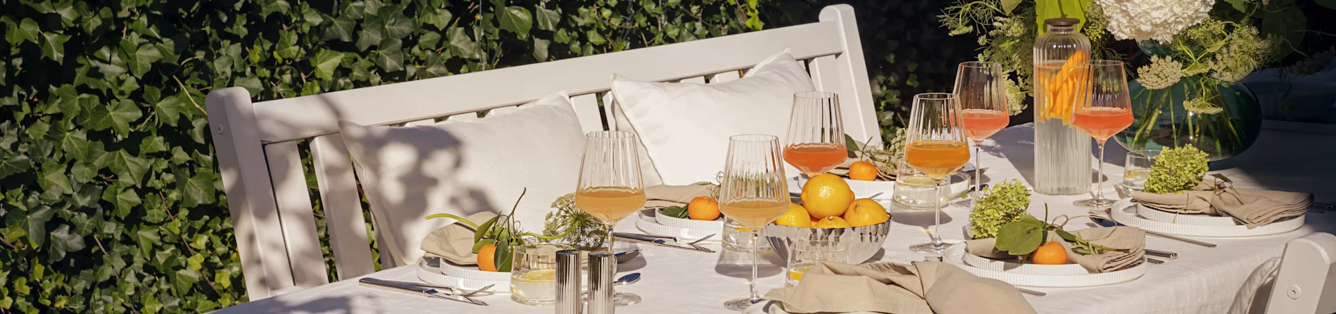 Outdoor-Tisch für ein Sommeressen mit weißen geriffelten Tellern, Leinenservietten, geriffelten Gläsern mit Getränken, Zitronen und Mandarinen.