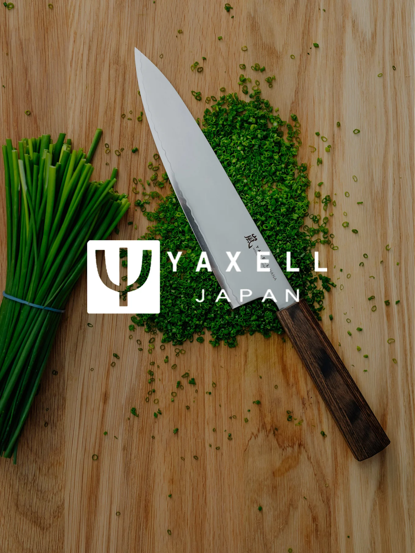 Yaxell Kochmesser, gehackter Schnittlauch und ein Bund Schnittlauch auf einem Holzschneidebrett mit Yaxell Japan Logo.