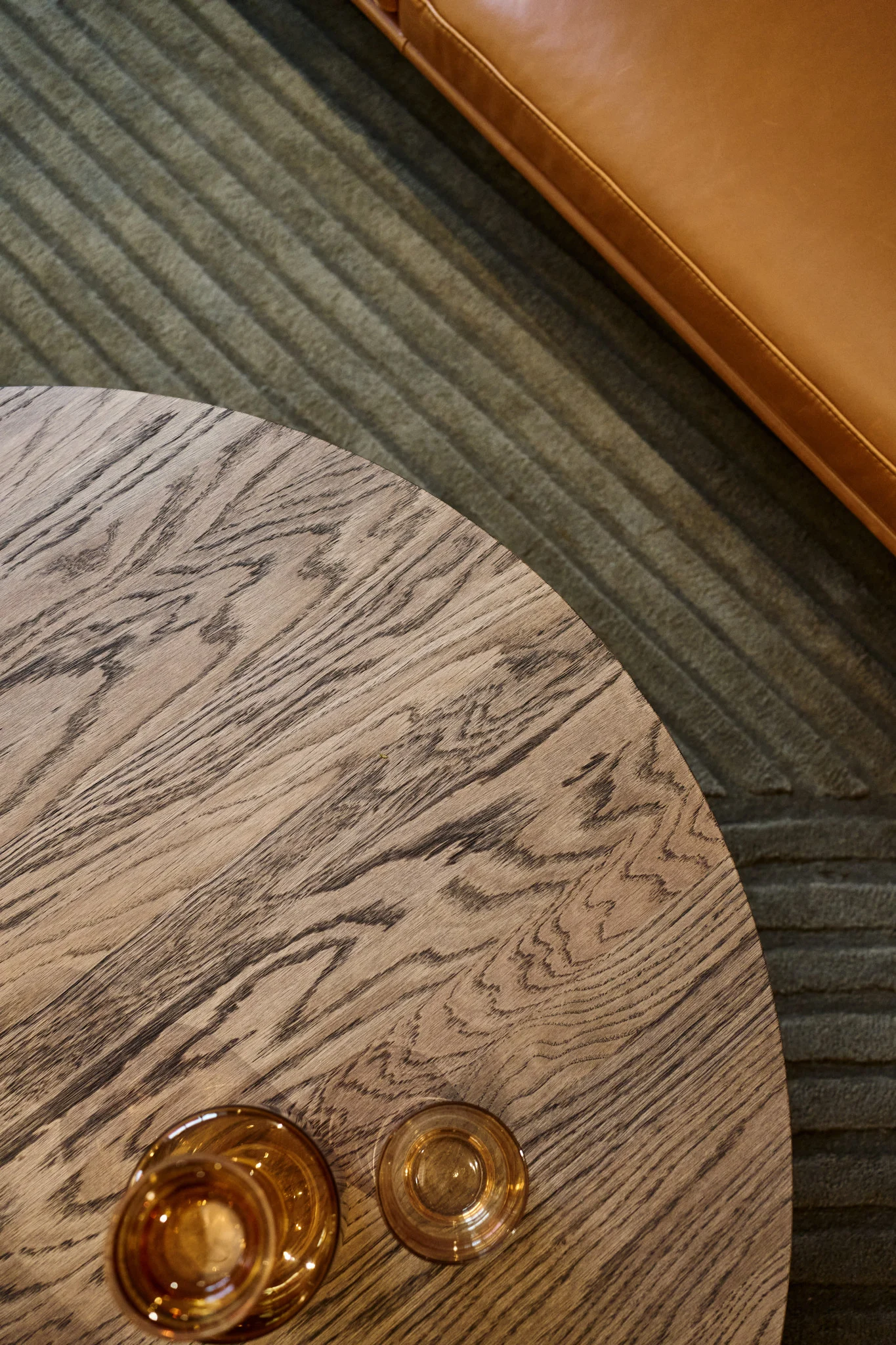 Vor einem Sofa steht ein Couchtisch mit dunkelbrauner Tischplatte, darauf stehen verschiedene bernsteinfarbene Gläser aus der Raise-Kollektion von Muuto.