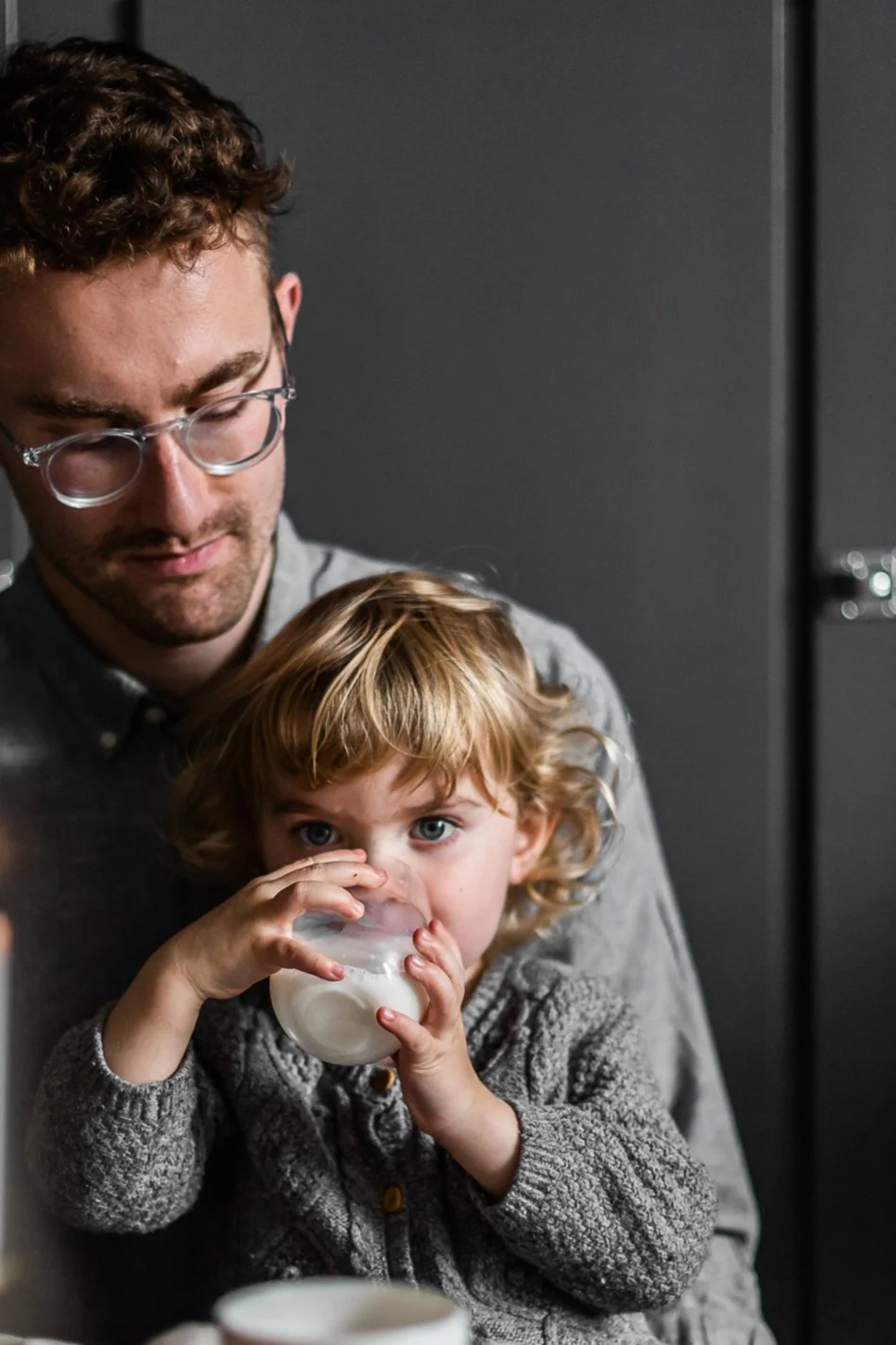 Gemeinsame Zeit ist sicherlich das wertvollste Geschenk zum Vatertag. Hier sehen Sie ein Kleinkind auf dem Schoß seines Vaters sitzen und aus einem Glas von Scandi Living trinken.