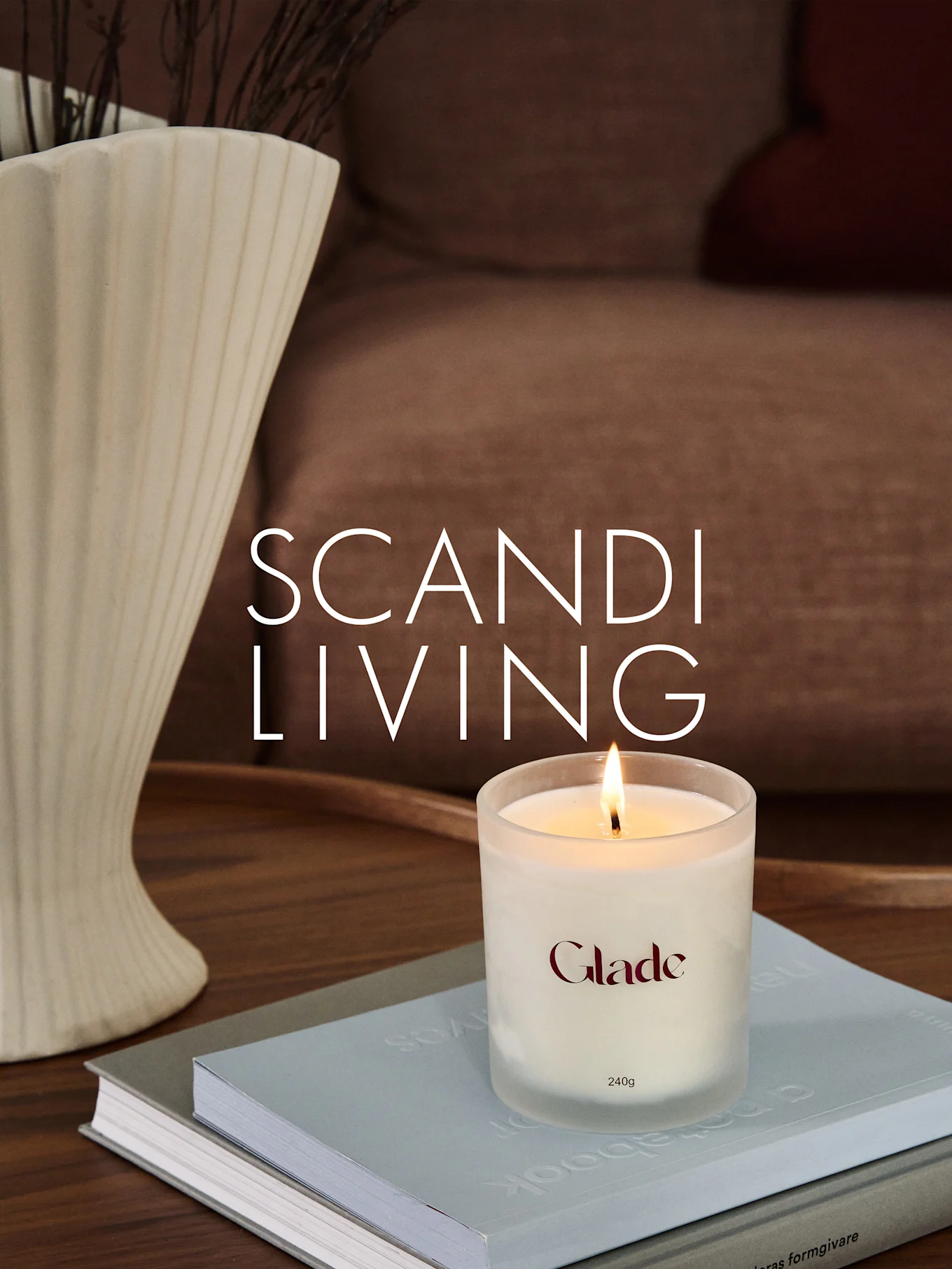 Eine brennende Glade-Kerze auf Büchern, neben einer geriffelten Vase mit Zweigen. Überlagerter Text: SCANDI LIVING.
