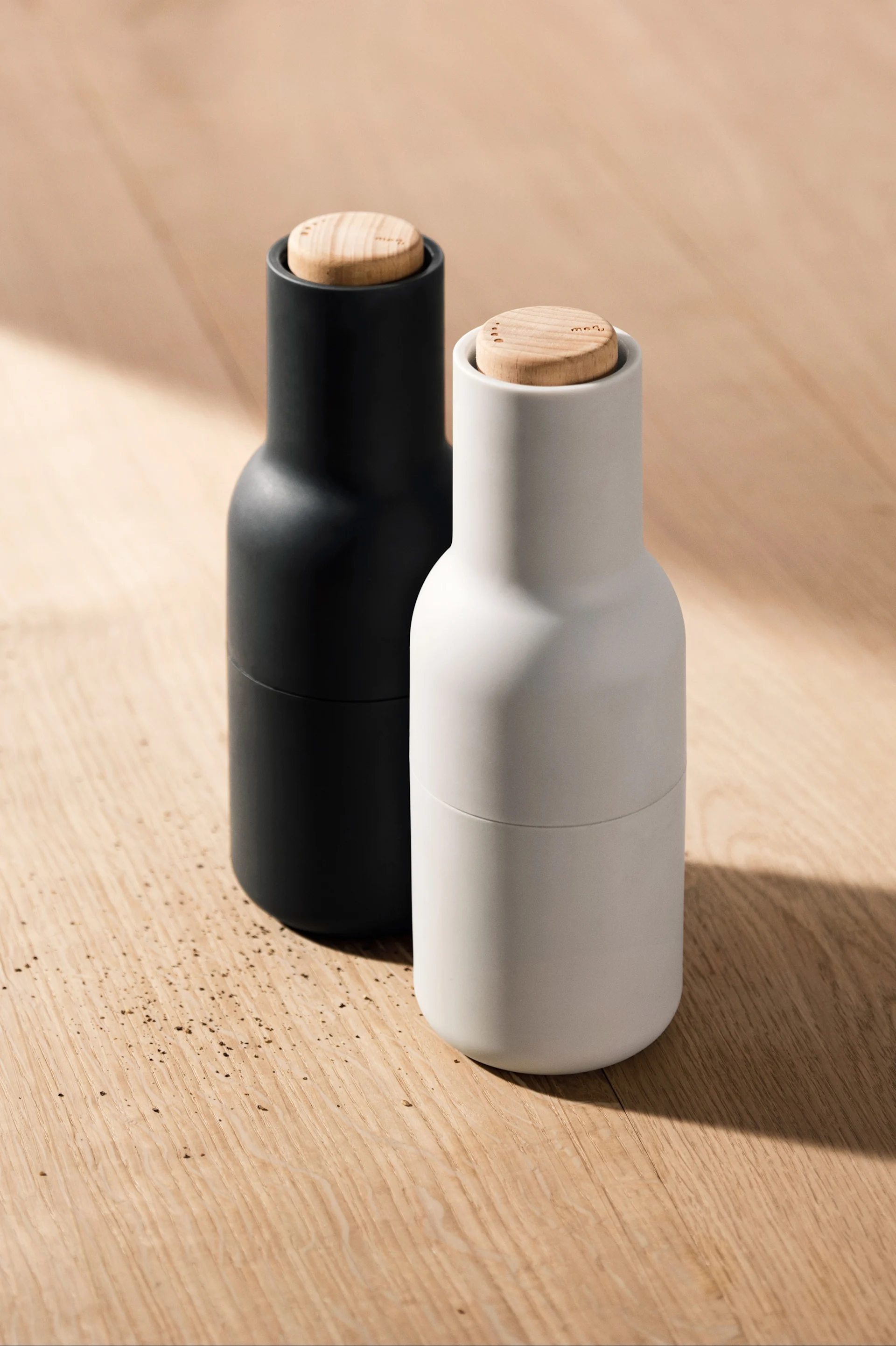 Hier sehen Sie zwei der Bottle Grinder von Audo Copenhagen auf einem Holztisch stehen.