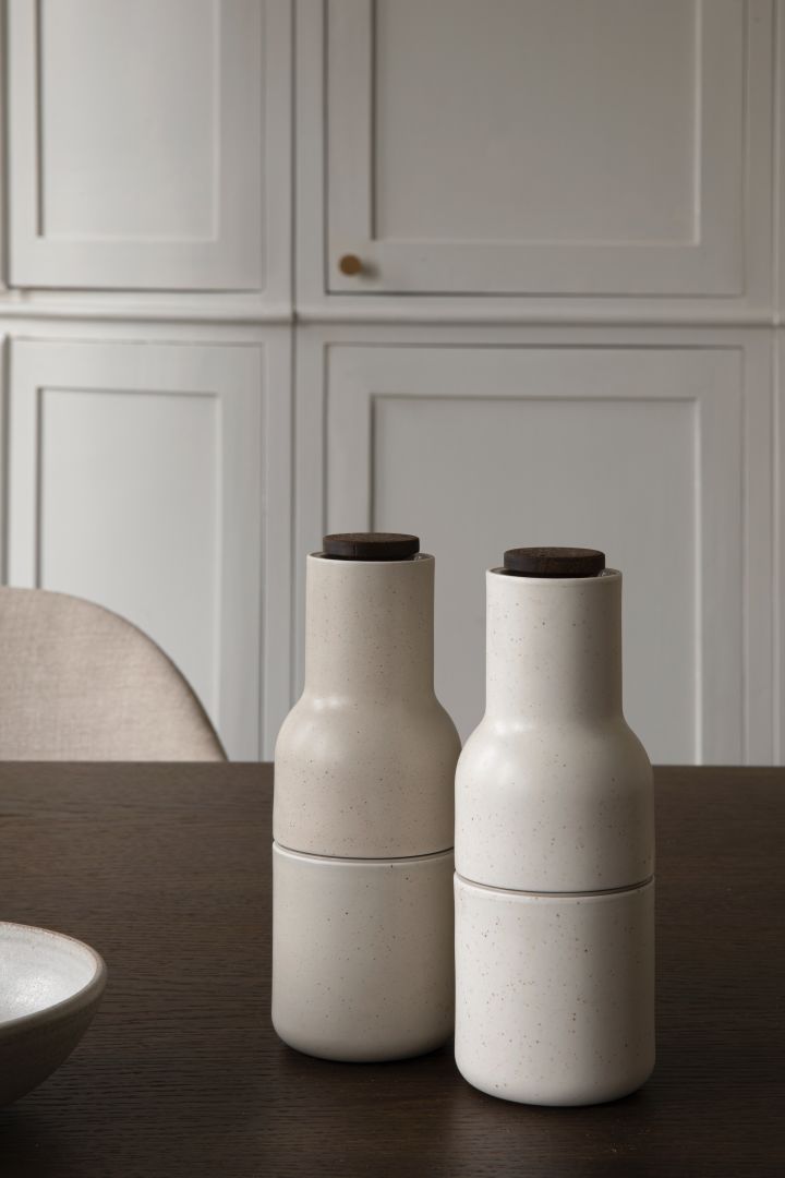 Hier sehen Sie zwei der hellen Keramik Bottle Grinder auf einem dunklen Holztisch stehen.