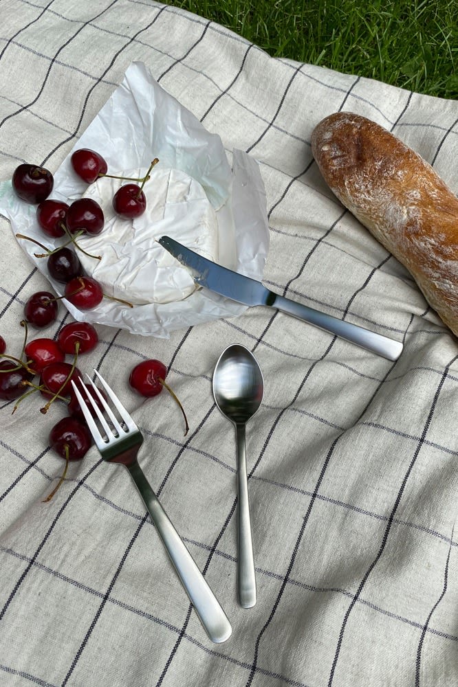 Hier sehen Sie das preisgekrönte Grand Prix-Besteck von Kay Bojesen auf einer Picknickdecke, zusammen mit Brot und Käse.