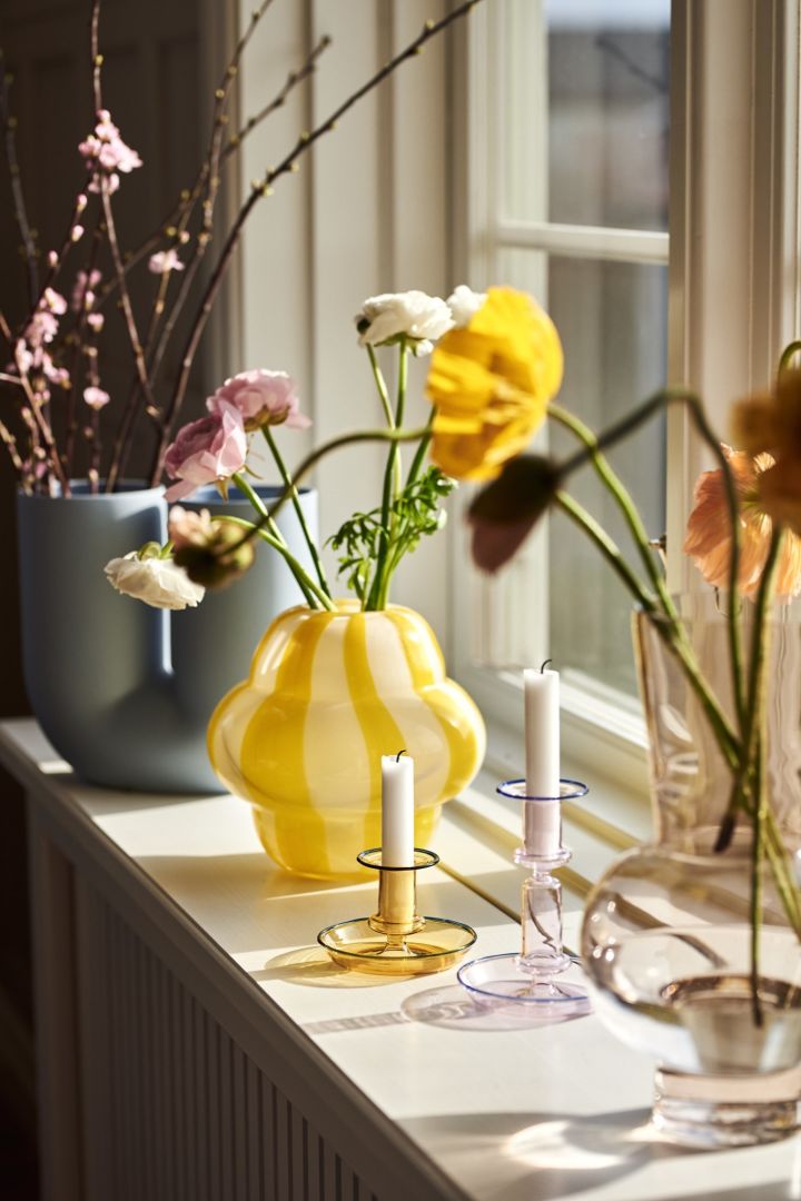 Frühlingserwachen: Die Curlie-Vase von Byon in einem knalligen Gelb steht zusammen mit anderen Vasen und Kerzenhaltern aus Glas auf der Fensterbank.