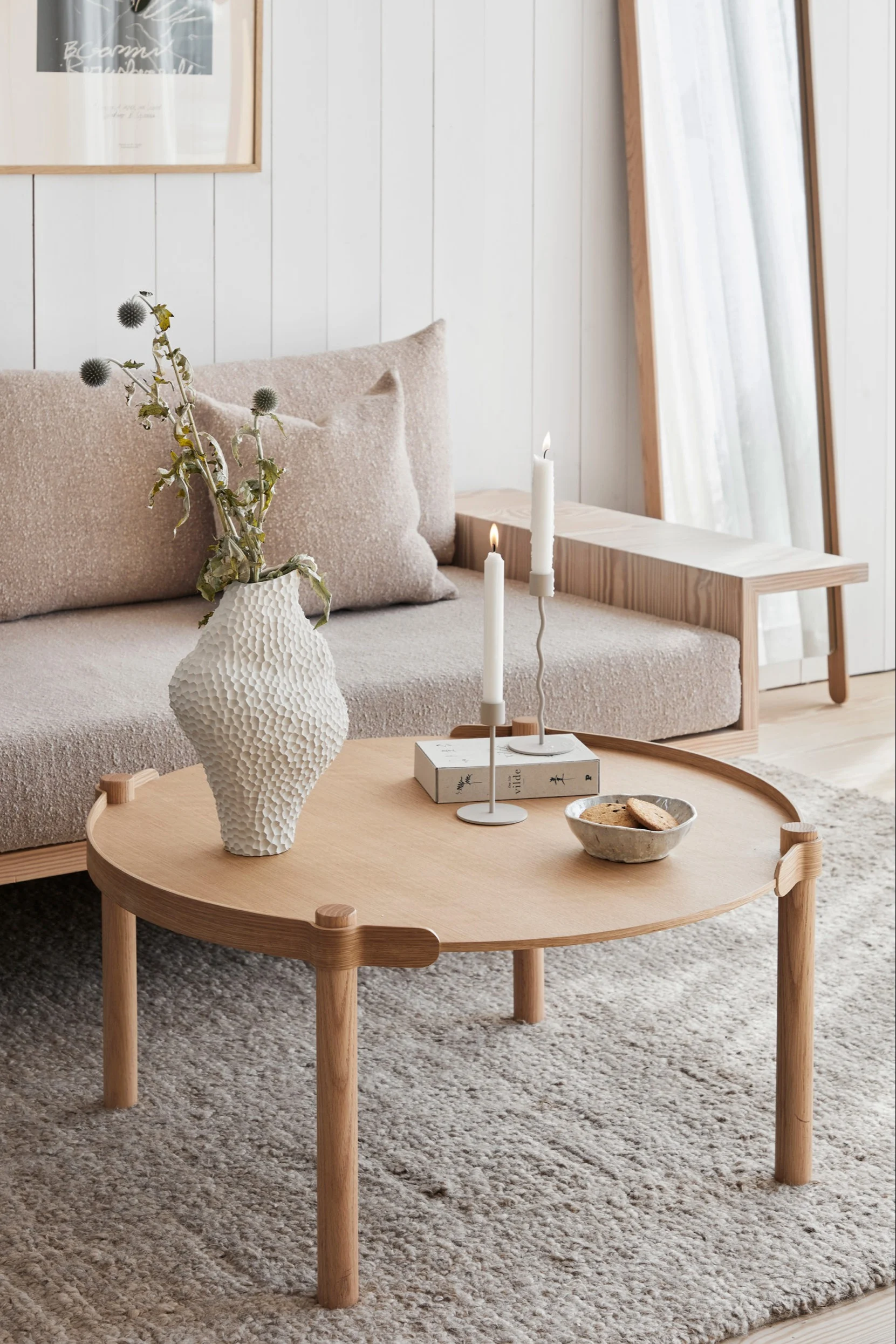 Ein cremefarbenes skandinavisches Wohnzimmer mit Produkten aus dem Sortiment von Cooee Design, darunter der Couchtisch Woody, die Isla Vase und der Curved Kerzenhalter.