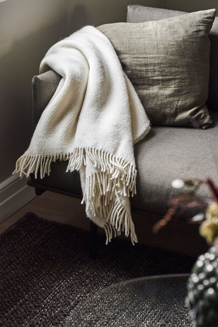 Eine kuschelige Decke eignet sich hervorragend als Muttertagsgeschenk. Hier sehen Sie die weiße Sandstone-Decke von Scandi Living über einer Couch liegen.