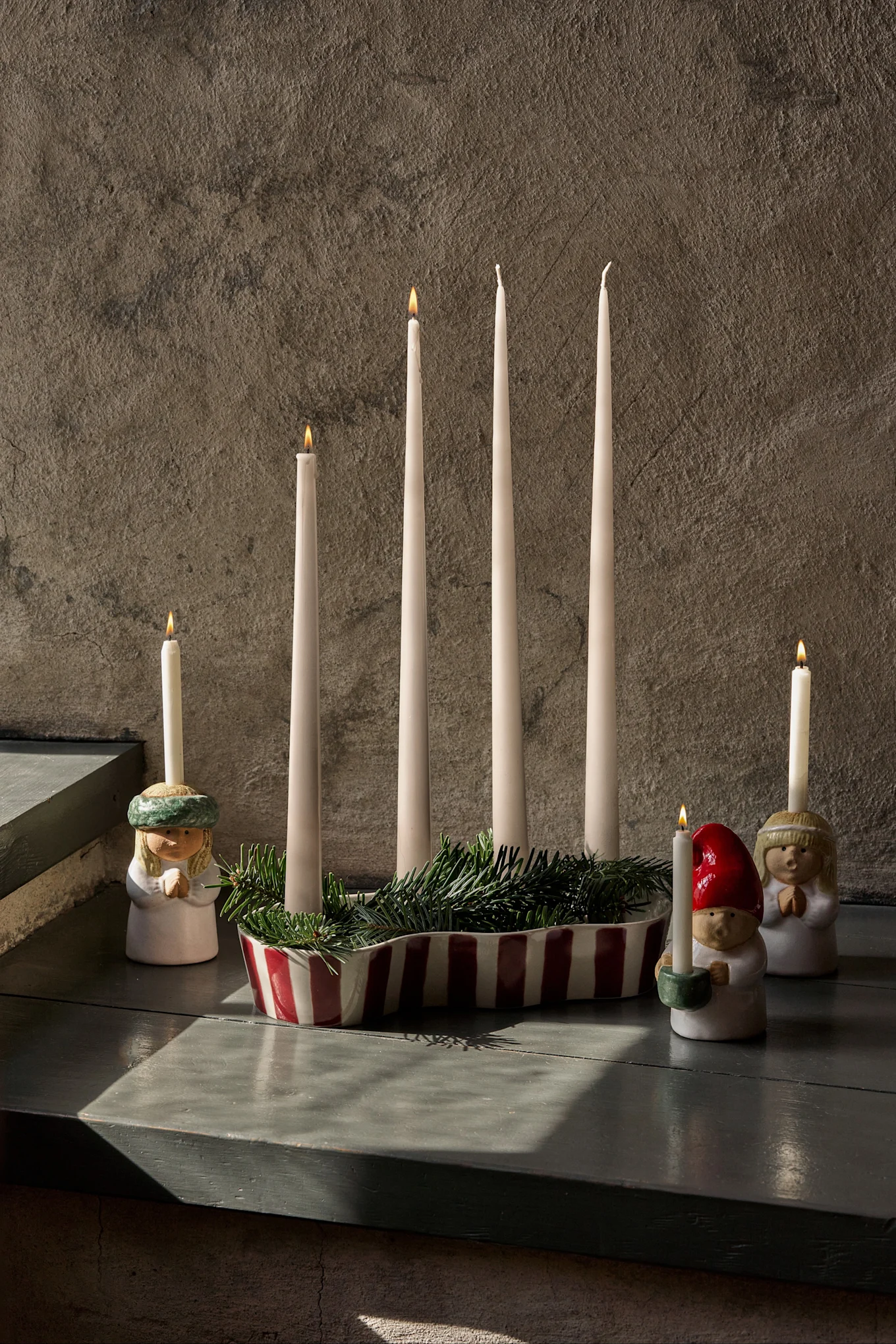 Adventsarrangement mit vier unangezündeten Kerzen, Tannengrün und drei Figuren mit angezündeten Kerzen.