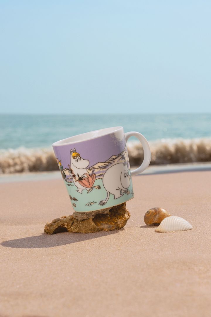 Die Mumin-Tasse Sommer 2025, "Beach Day" steht an einem Sandstrand.