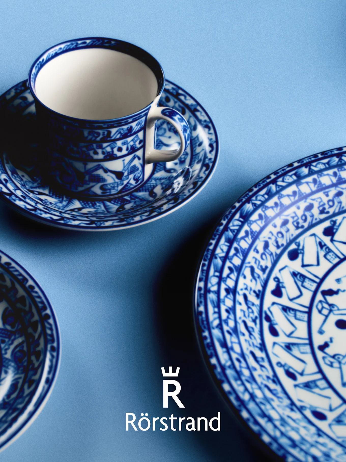 Blau-weiß gemusterte Teetasse, Untertasse und Teller auf hellblauem Hintergrund, mit Rörstrand-Logo.