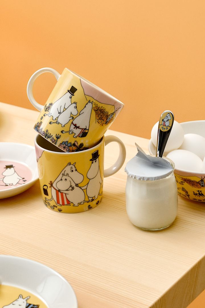 Zwei Family time Mumin Tassen stehen gestapelt auf einem gedeckten Frühstückstisch.
