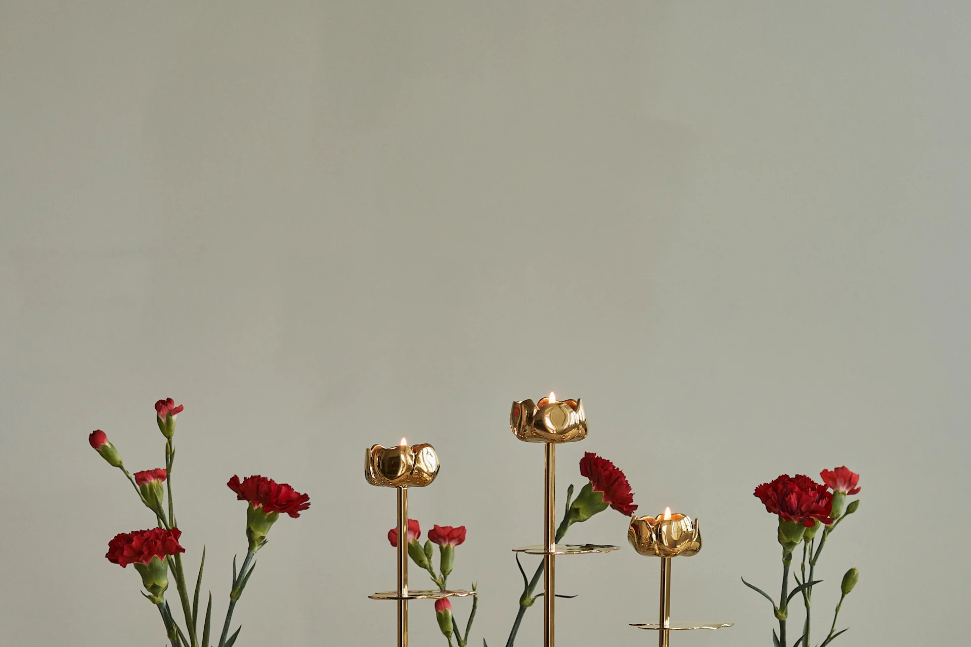 Goldene blumenförmige Kerzenständer mit brennenden Kerzen und roten Nelken.