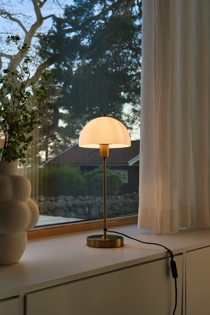 Zur perfekten Lichtplanung gehört auch die Gestaltung der Fensterbank. Hier wurde das Fensterbrett mit der Balloon Vase von Louise Roe und der Vienda Tischlampe von Herstal dekoriert.
