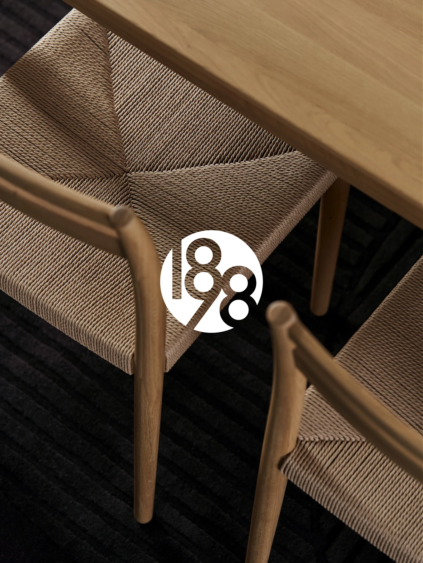 Zwei Holzstühle mit geflochtenen Sitzen, ein Holztisch und ein dunkler Teppich. Weißes '188' Logo als Überlagerung.
