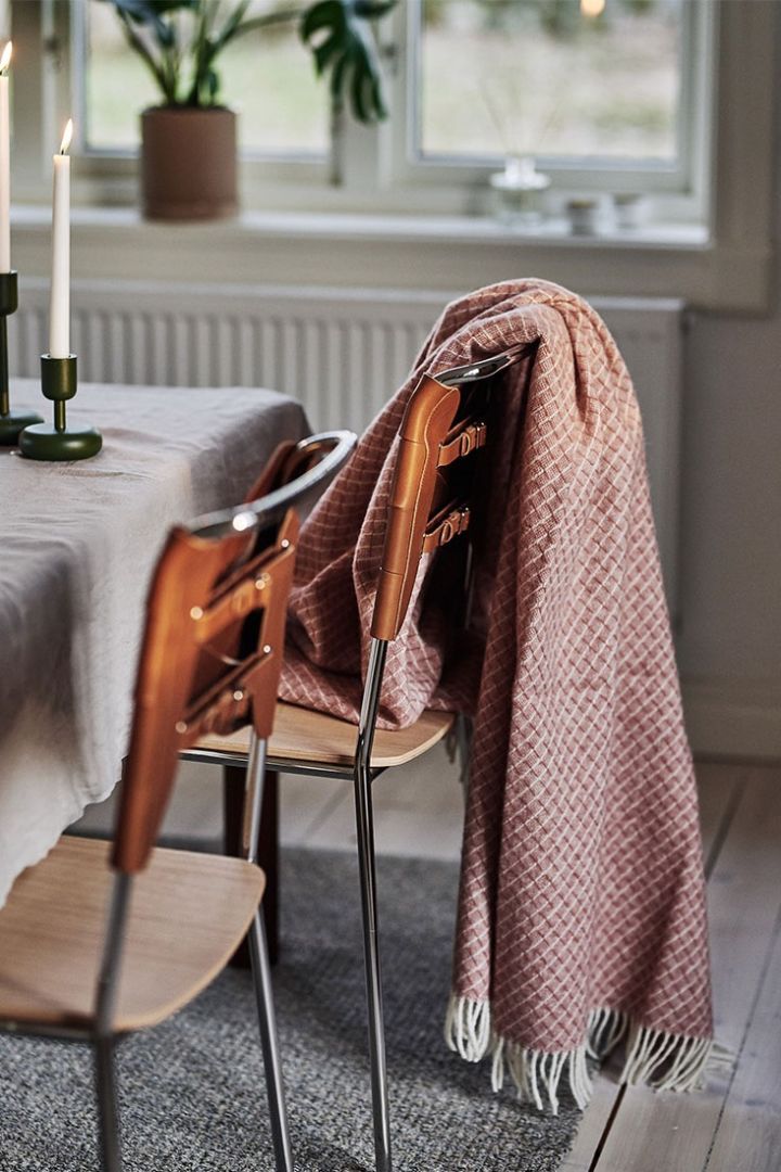 Die Wicker Woldecke in dusty Rose von Scandi Living hängt über einem braunen Esszimmerstuhl von Design House Stockholm in einem retro-inspirierten Essbereich.