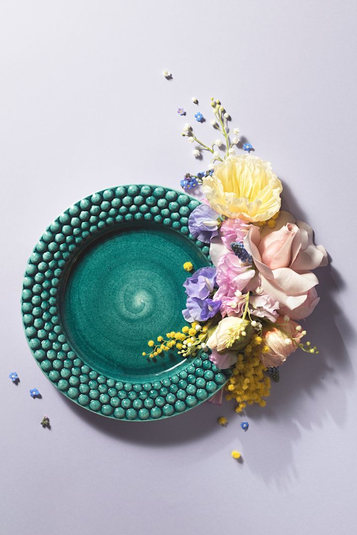 Ein Teller aus der Bubbles-Kollektion in der Farbe Ocean von Mateus, der für ein Foto kunstvoll mit Blumen in Szene gesetzt wurde.