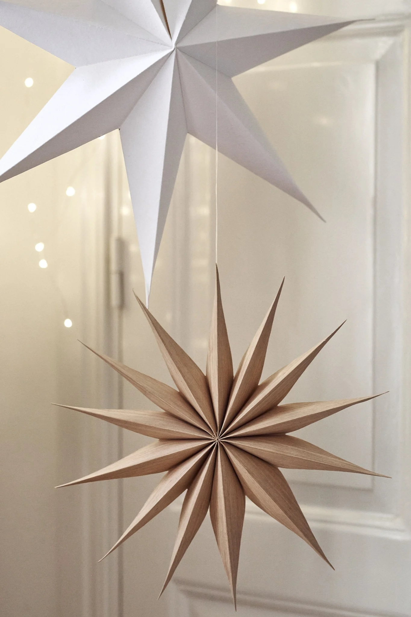 Venok Weihnachtsstern von Broste Copenhagen hängt umgeben von anderen Adventssternen und Licherketten.