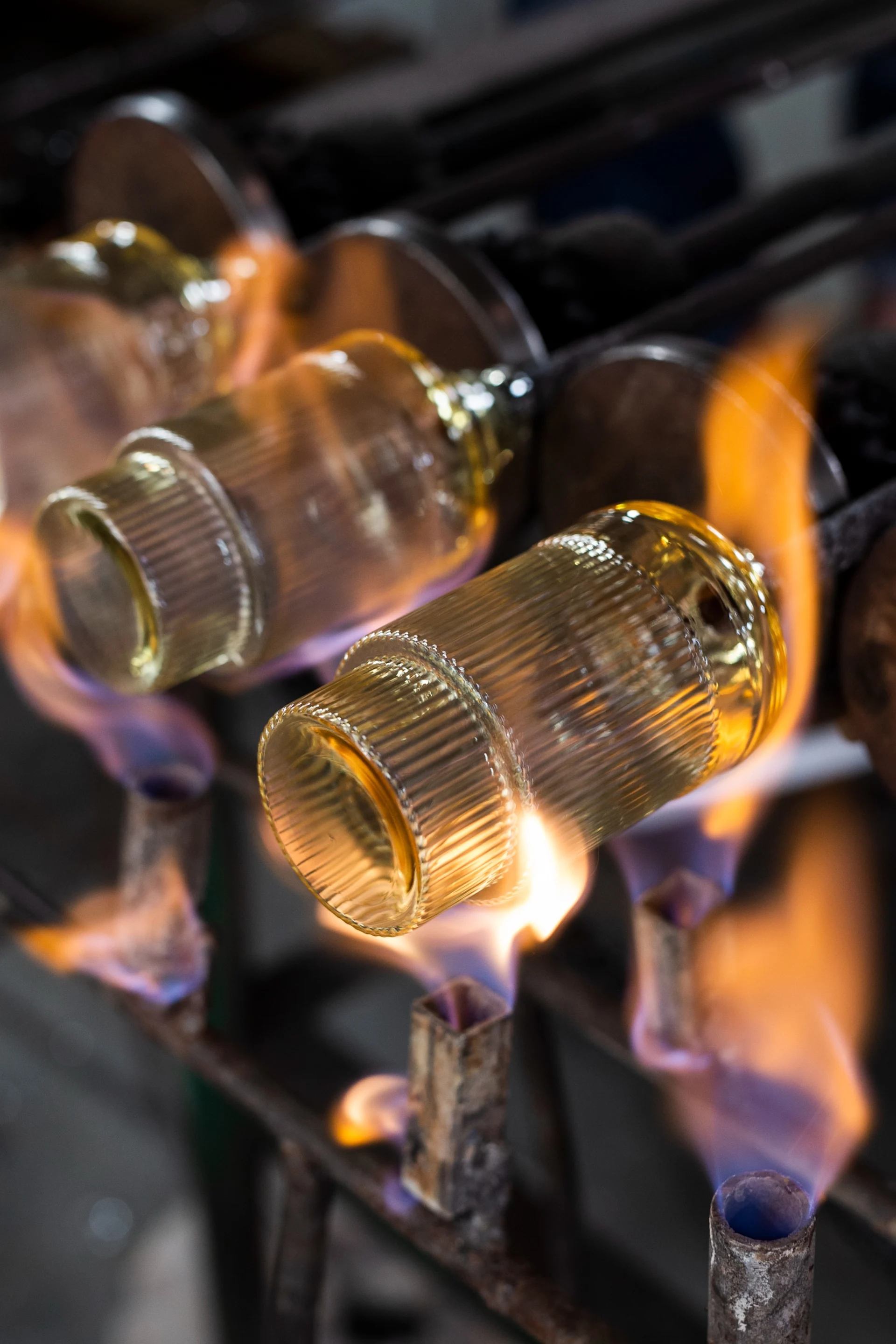 Gerippte goldene Glasobjekte werden von orangefarbenen und blauen Flammen auf einem Metallgestell erhitzt.