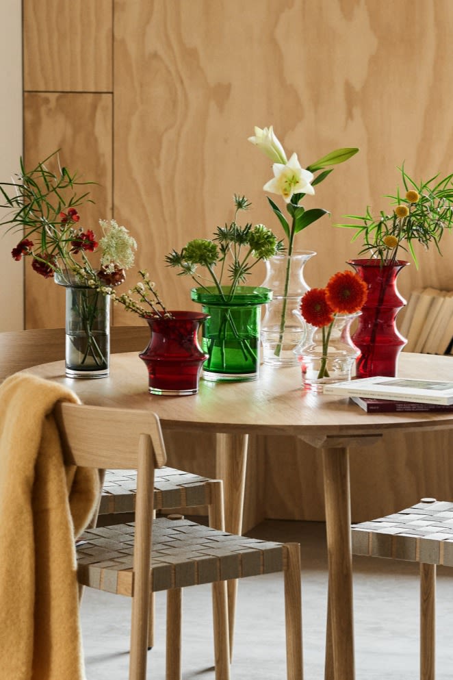 Frühlingserwachen: Hier sehen Sie eine Sammlung von Kosta Boda-Vasen aus klarem, rotem und grünem Glas auf einem Esszimmertisch mit frischen Schnittblumen stehen.