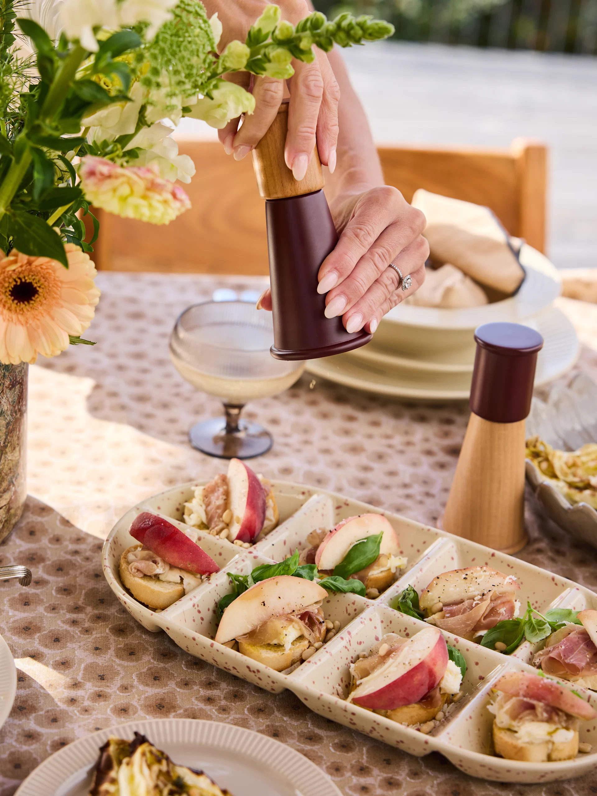 Hände mahlen Pfeffer auf Crostini-Platte mit Pfirsichen, Prosciutto, Käse, Pinienkernen, Basilikum.