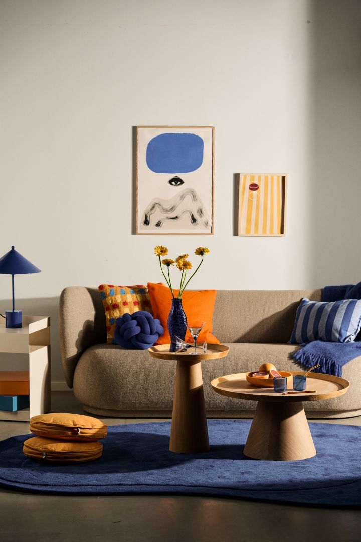 Dekorieren Sie nach den skandinavischen Wohntrends 2024 und verwenden Sie viele Farben und Muster, die Sie miteinander kombinieren können. Hier sehen Sie ein Wohnzimmer mit blauem, orangefarbenem und gelbem Dekor. 