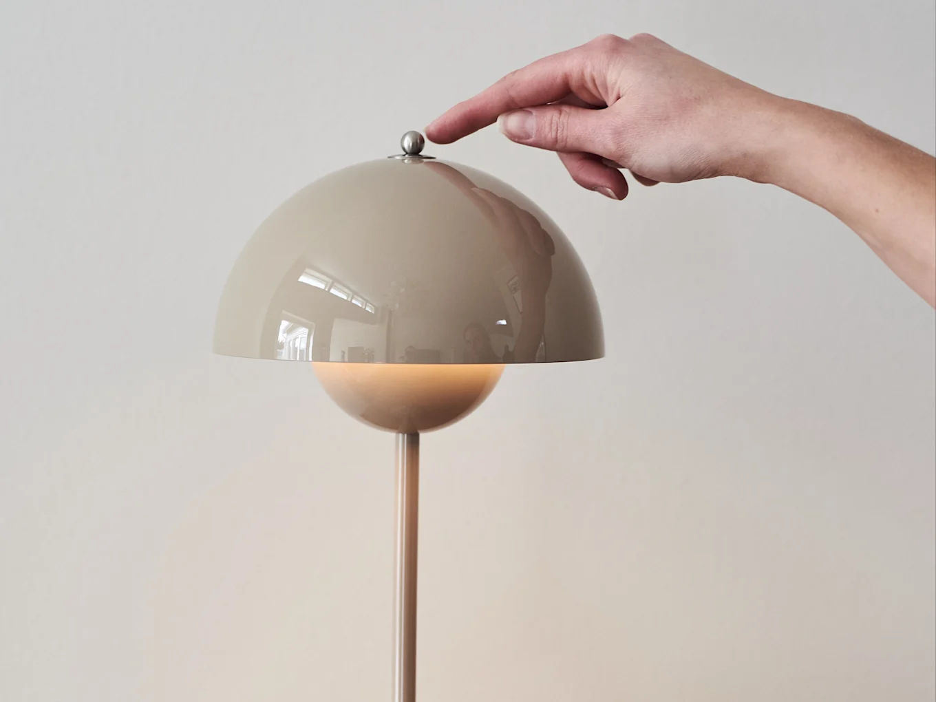 Hand drückt einen metallischen Knopf auf einer beigefarbenen, kuppelförmigen Lampe, die ein warmes Licht abgibt.
